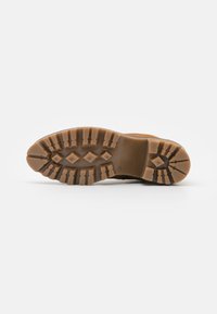 Suela de bota marrón robusta con surcos profundos, patrones hexagonales y de diamante, hecha de goma duradera, diseñada para ofrecer tracción en diversas superficies.