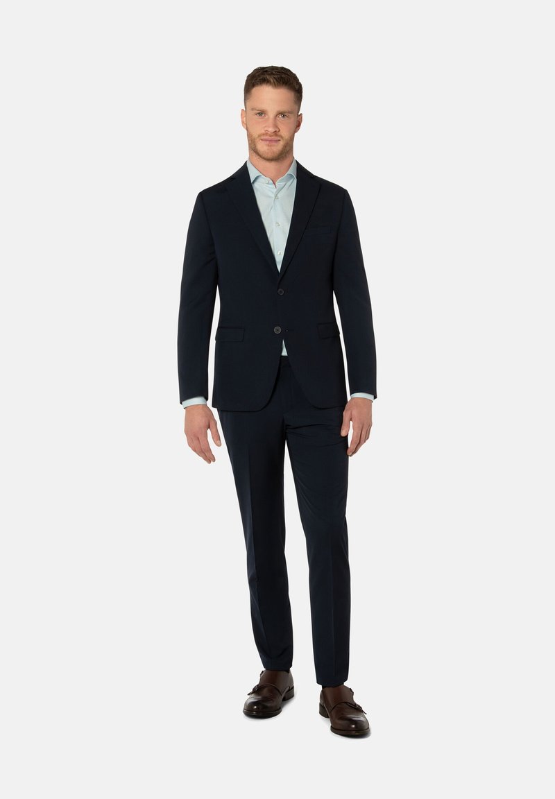 Navy suit with a two-button blazer and matching trousers, paired with a light blue shirt and brown leather shoes. Smooth fabric texture.
