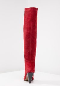 Rode suede kniehoge laars met een spitse neus en een zwarte stilettohak. Heeft een zijrits en een gladde textuur.