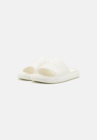 White slide sandals made of rubber with an open-toe design. Features embossed logo on the upper and textured sole. Minimalist style.