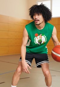 Πράσινη αμάνικη φανέλα με το γραφικό "Boston Celtics", μαύρα σορτς με άσπρες ρίγες και μια μπάλα μπάσκετ, σε γυμναστήριο με ξύλινους τοίχους.