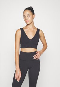 Black cropped athletic bra with a deep V-neck and thick shoulder straps, paired with high-waisted black leggings, featuring a smooth texture.