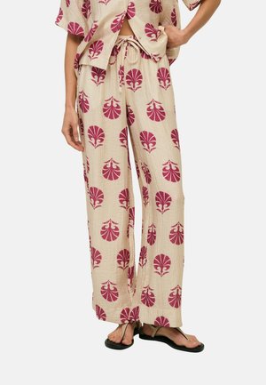 Pantalones sueltos beige y camiseta de manga corta a juego con estampado floral en rosa oscuro, combinados con sandalias tipo tanga negras sobre fondo neutro.