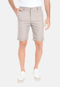 Pantaloni corti beige realizzati in tessuto leggero, con una parte frontale piatta, passanti per la cintura e design con risvolto. Indossati con sneakers bianche.