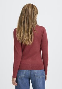 Roter Pullover mit langen Ärmeln und tailliertem Design, geripptem Saum und Bündchen, kombiniert mit hochtaillierten blauen Jeans. Glatte Textur, keine sichtbaren Muster.