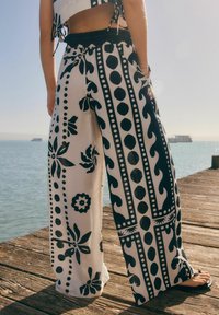 Pantalones de pierna ancha con un patrón floral en blanco y negro, que presentan franjas y puntos llamativos, hechos de un material ligero y transpirable.