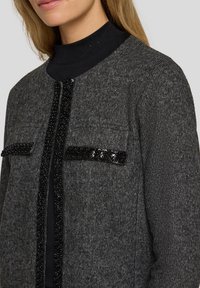 Graue Strickjacke mit Perlenverzierungen entlang des vorderen Verschlusses und der Taschen; verfügt über ein strukturiertes Finish und einen runden Ausschnitt.