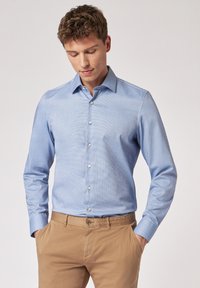 Camicia a maniche lunghe blu chiaro con un motivo a quadri sottile, colletto button-down e bottoni bianchi, abbinata a pantaloni beige.