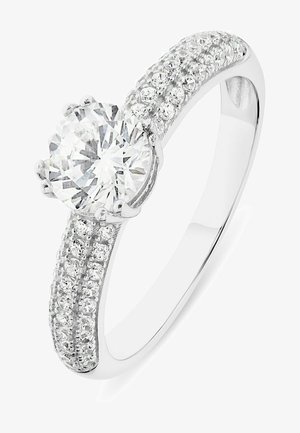 Bague en or blanc mettant en valeur un grand diamant rond central, entouré de petits diamants sur la bande, créant un effet scintillant.
