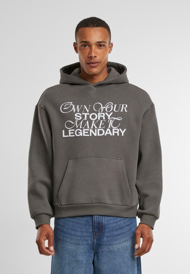 Szary hoodie z dużym białym nadrukiem na plecach, który brzmi "ZARZĄDZAJ SWOJĄ HISTORIĄ, UCZYŃ JĄ LEGENDARNĄ". Kieszeń kangurka z przodu, ściągacze na rękawach.