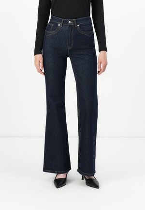 Jean flare bleu marine avec taille haute, doté de deux poches avant, de coutures jaunes et d'une fermeture à bouton. Texture lisse.