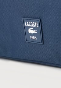 Sinine tekstuuriga kangas tumesinise Lacoste Pariisi logomärgiga, kus on valge krokodillikuju.