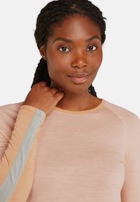 Maglietta a maniche lunghe di colore rosa chiaro con un accento blu a contrasto sulle maniche; presenta un collo rotondo e un discreto dettaglio del logo.