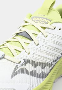 Witte hardloopschoen met limoen groene accenten. Mesh stof, textuur overlays en gestructureerde details. Reflecterende veters en logo-label zichtbaar.
