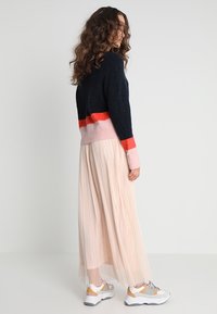 Pull en maille rayé bleu marine et rouge, accents roses, associé à une jupe plissée beige fluide et des baskets blanches épaisses.