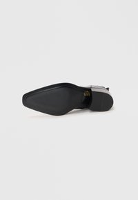 Schwarze Schuhsohle mit abgerundeter Form, strukturiertem Gummiunterboden und einem leichten Absatz. Verfügt über ein geprägtes Markenlogo im Bereich des Absatzes.