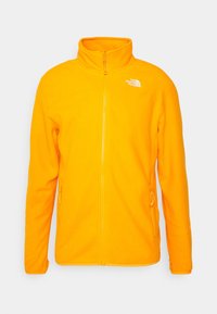 Chaqueta de forro polar naranja brillante con cremallera frontal completa, dos bolsillos laterales con cremallera y el logotipo blanco de "The North Face" en el pecho.