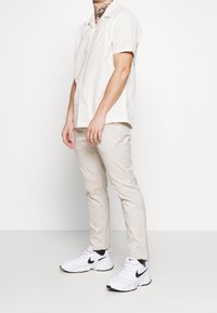 Kortärmad, off-white skjorta med knappar och avslappnad passform; matchad med ljus beige randiga byxor och vita träningsskor.