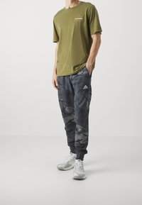 Olivgrön bomulls-t-shirt med logotyp på bröstet; grå camouflagemönstrade sweatpants; vita sneakers med grå accenter; strömlinjeformat design, avslappnad passform.