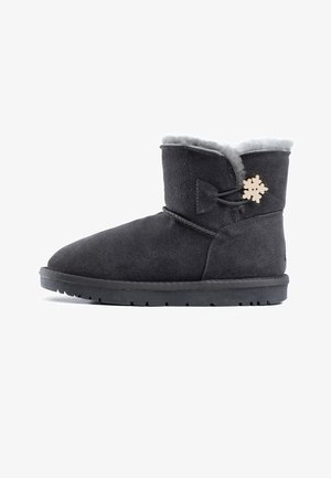 Zwarte suède enkellaars met een pluche grijze bontvoering, een ronde neus en een decoratieve houten sneeuwvlokaccent aan de zijkant. Platte rubberen zool.
