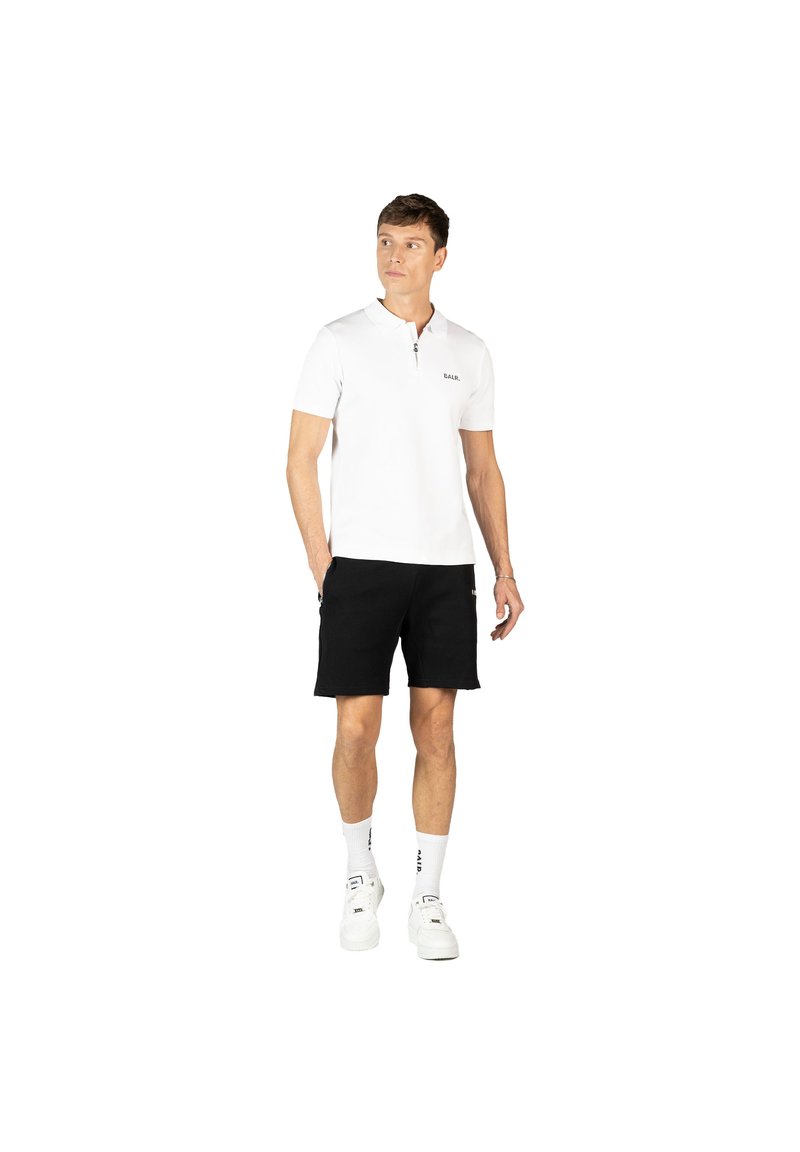 Polo bianca con mezza cerniera e logo discreto sul petto, abbinata a pantaloni corti neri e sneaker bianche, che migliora un look casual.