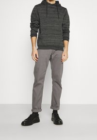 Felpa grigia a righe con tasca frontale, abbinata a pantaloni grigi chiari arrotolati sui polsini. Sneakers nere completano l'outfit.