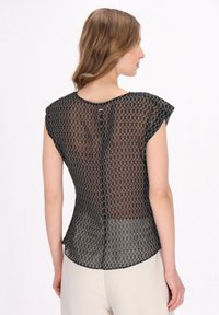 Zwarte doorschijnende top met een geometrisch patroon, cap sleeves, ronde halslijn en een knoopdetail op de rug. Soepele textuur, ontspannen pasvorm.