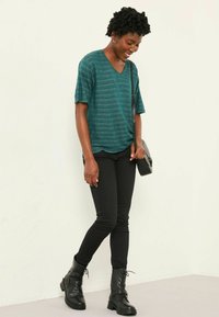 Teal v-neck t-shirt with short sleeves, paired with black skinny jeans and black lace-up ankle boots. Minimalist crossbody bag detail.