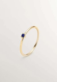 Anillo de oro con una banda delgada, que presenta una gema azul redonda engastada en un montaje de cuatro garras, acabado suave y diseño sencillo.