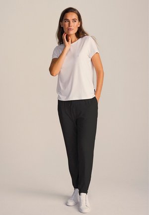 Hvid kortærmet t-shirt parret med sorte joggingbukser; joggingbukserne har snore i taljen og er indsnævret ved anklerne, med hvide sneakers.