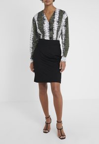 Dlouhý rukáv blůza s abstraktním vzorem v zelené a bílé barvě a hlubokým výstřihem do V, doplněná o úzkou černou tuhou sukni a černé sandály na podpatku.