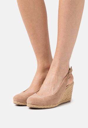 Chaussures compensées en suède beige avec un dos ouvert et une bride à la cheville, doté d'une semelle en jute tissée et d'un design à bout arrondi.