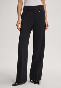 Zwarte broek met wijde pijpen van een zachte, nette stof. Voorzien van een knoopsluiting, riemlussen en een subtiele vierkante accent op de tailleband.