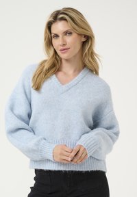 Hellblauer V-Ausschnitt-Pullover aus flauschigem, strukturiertem Strickmaterial mit gerippten Bündchen und Saum, der eine lockere Passform und überschnittene Schultern aufweist.