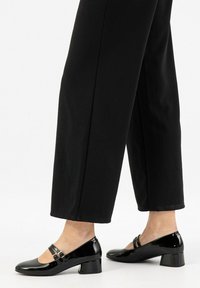 Černé lakované kožené lodičky s kulatou špičkou a dvěma úzkými pásky přes přední část. Design na bloku, hladký povrch a lesklý finish.