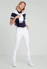 Marineblaues Polohemd mit weißen Streifen, weiße Hose und weiße Schuhe. Ein weißer Pullover über die Schultern drapiert mit roten und blauen Akzenten.