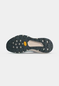 Semelle de chaussure robuste noire et beige avec des motifs de profondeur et un petit logo Vibram jaune au centre.