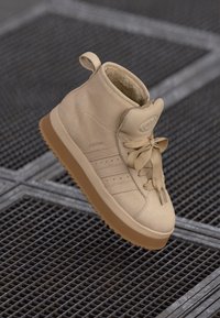 Sneaker alta beige in suede, con colletto imbottito, lacci ampi e suola in gomma texturizzata con design a tre strisce.