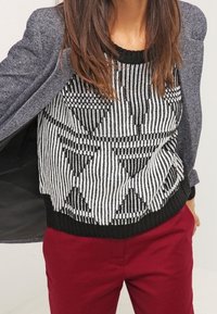 Svart och vit geometrisk mönstrad tröja med texturerad stickad design, tillsammans med vinröda byxor och en grå kavaj.