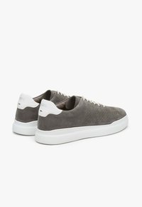 Szare zamszowe sneakersy z perforowanym wzorem i białymi gumowymi podeszwami, z tonującymi sznurowadłami i kontrastującymi akcentami na pięcie.