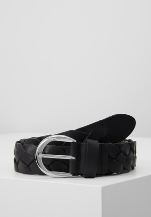 Ceinture en cuir noir tressé avec boucle en métal argenté arrondie, posée enroulée sur une surface blanche sur fond gris clair.