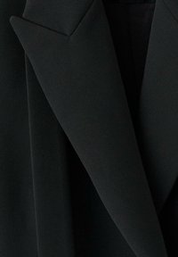 Czarna marynarka z ostrymi, kątowymi klapami i teksturowaną tkaniną. Projekt jest czysty i nowoczesny, o dopasowanym kroju.