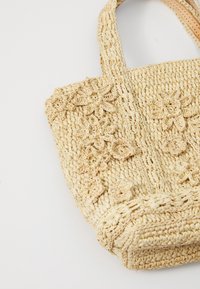 Pletená taška z béžové slámy s květinovou háčkovanou výzdobou a dvěma pevnými držadly. Obdélníkový tvar s texturovaným povrchem.