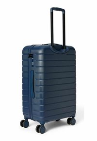 Valise rigide bleu marine avec surface texturée, rainures verticales, poignée télescopique réglable et quatre roues noires pour la mobilité.