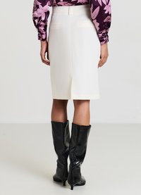 Weißer knielanger Bleistiftrock mit Schlitz hinten, kombiniert mit glänzenden schwarzen knielangen Stiefeln. Glatte Textur und maßgeschneiderte Passform.