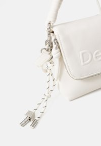 Borsa bianca in pelle sintetica con chiusura a zip, finitura texturizzata e manico corto intrecciato. Presenta accessori in argento e un dettaglio decorativo in corda.
