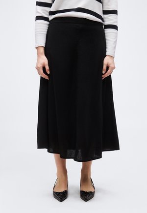 Inimene, kellel on must midi seelik, mustad terava ninaga kingad paeltega ja valge kampsun mustade horisontaalsete triipudega.