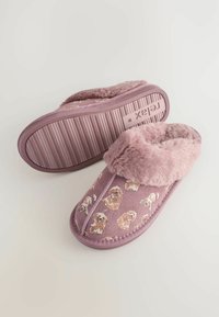 Rožinės slankiosios šlepetės, pagamintos iš švelnaus audinio su pūkuotu apvadu, turinčios šuns spaudą. Raukšlėta padas, užtikrinantis sukibimą. Visur švelni tekstūra.