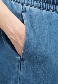 Χέρι που έχει τοποθετηθεί στην πλαϊνή τσέπη ανοιχτόχρωμων τζιν παντελονιών με ελαστική μέση.