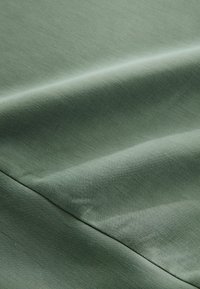Light green fabric with a smooth texture, featuring folds and creases, highlighting its soft, matte surface and subtle sheen.